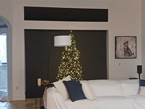 A Christmas tree set in front of a large, covered window